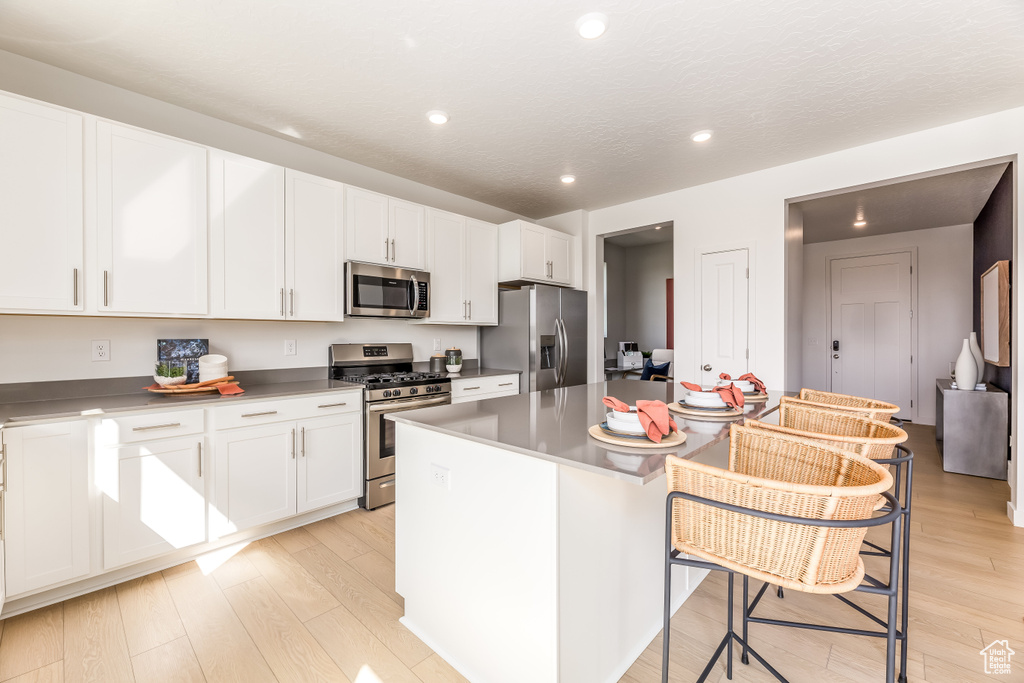 Kitchen featuring white cabinets, stainless steel appliances, a center island, and a kitchen breakfast bar