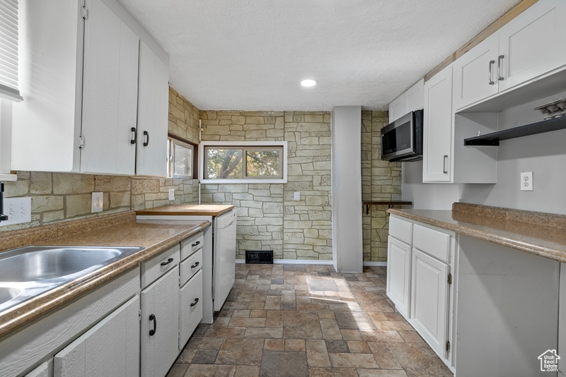 Kitchen featuring sink, white cabinets, dishwasher, and a textured ceiling