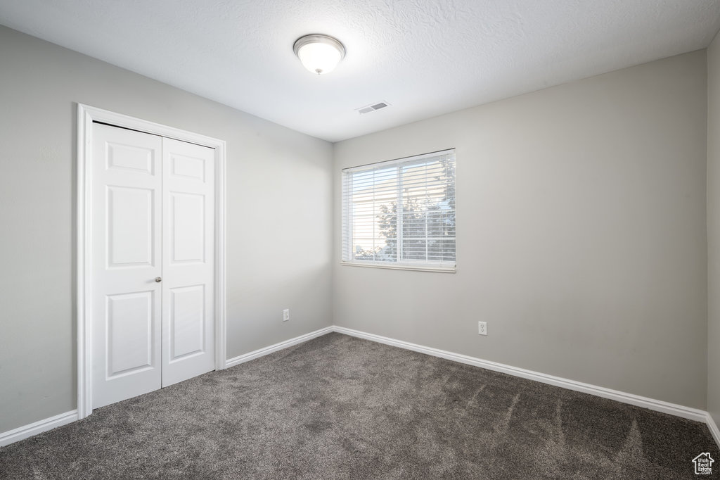 Unfurnished bedroom with dark colored carpet, a textured ceiling, and a closet