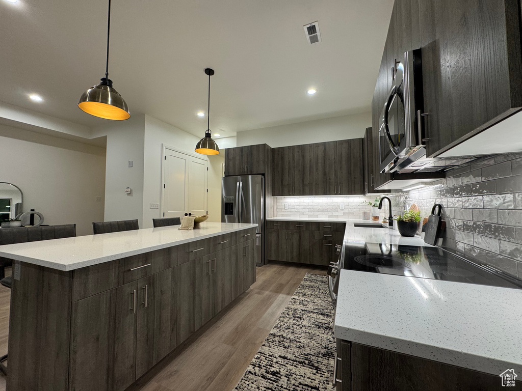 Kitchen with stainless steel appliances, a kitchen island, sink, and decorative light fixtures