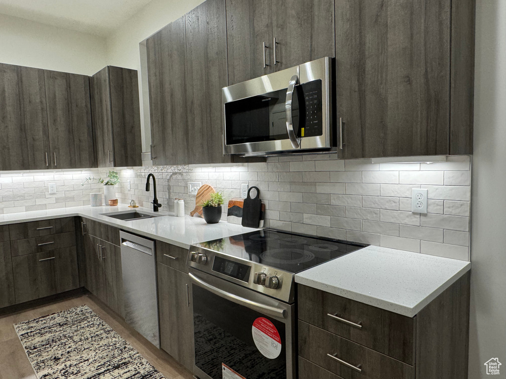 Kitchen with sink, dark brown cabinets, stainless steel appliances, tasteful backsplash, and light stone counters