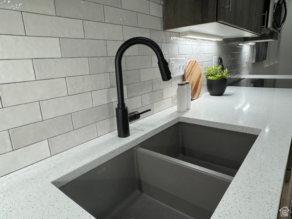 Room details with dark brown cabinetry, light stone countertops, sink, and backsplash