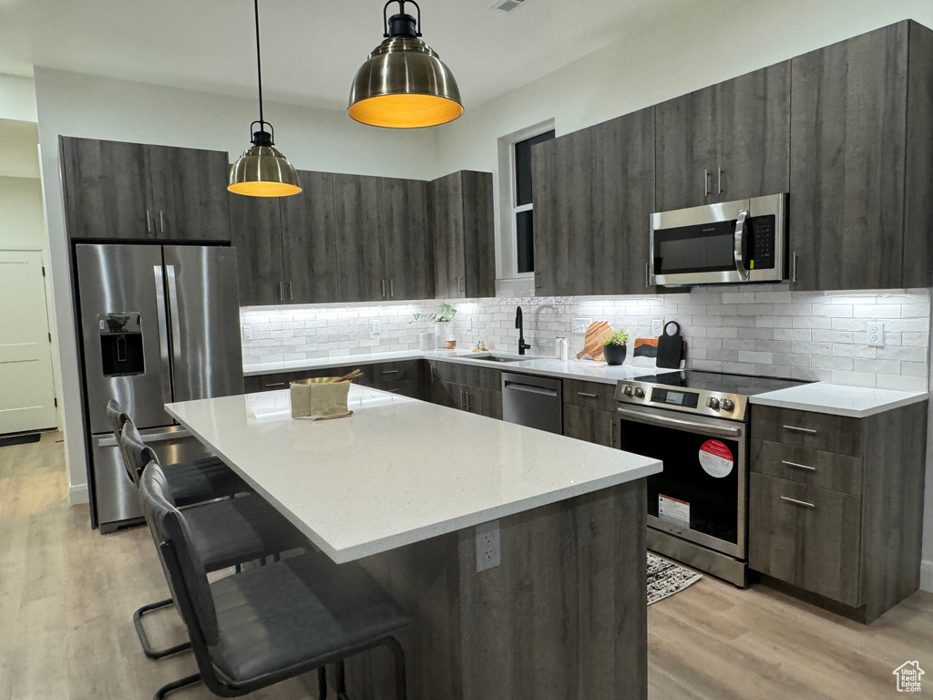 Kitchen featuring a breakfast bar, a center island, hanging light fixtures, light hardwood / wood-style flooring, and appliances with stainless steel finishes