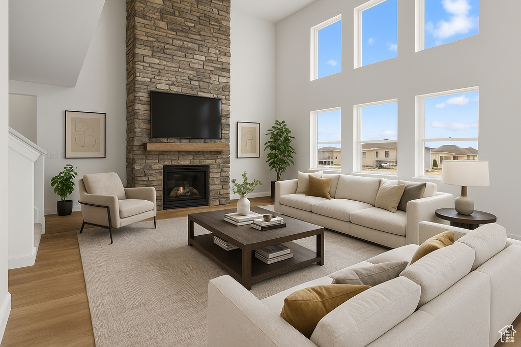 Living area featuring light wood-type flooring, baseboards, a towering ceiling, and a stone fireplace