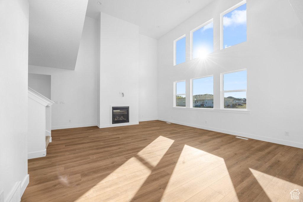 Unfurnished living room with a towering ceiling and light wood-type flooring