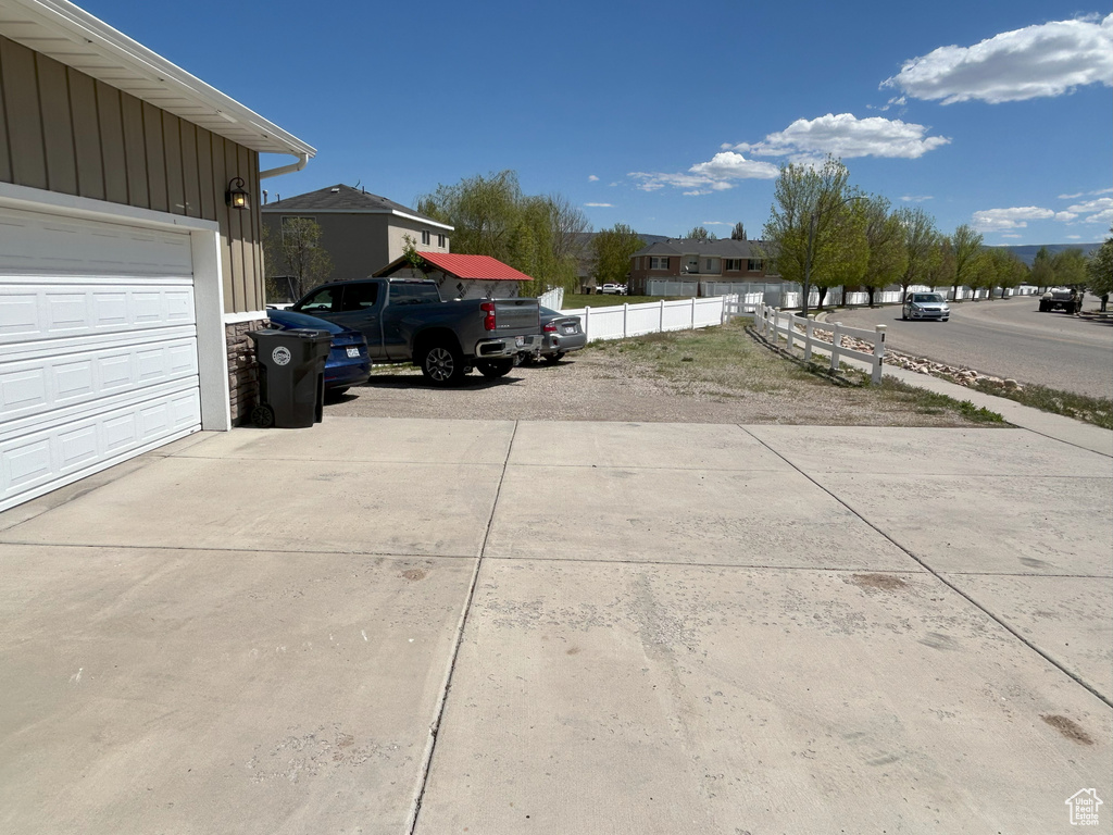 View of vehicle parking featuring fence, a garage, and driveway