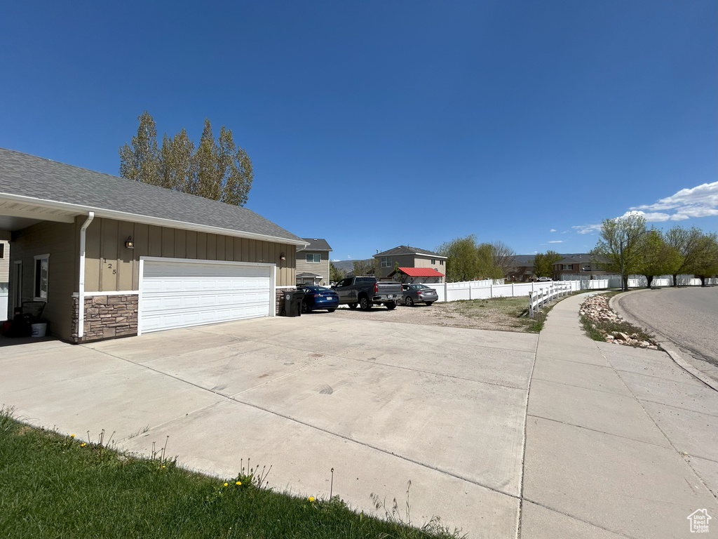 View of side of home featuring board and batten siding, fence, a garage, driveway, and roof with shingles