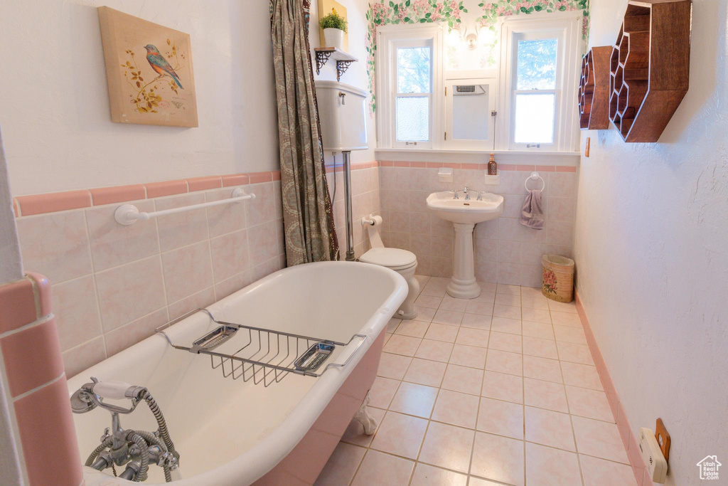 Bathroom featuring tile patterned floors, toilet, a washtub, sink, and tile walls