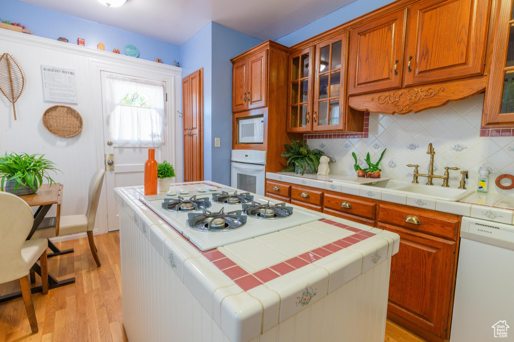 Kitchen with tile counters, decorative backsplash, light wood-type flooring, and white appliances