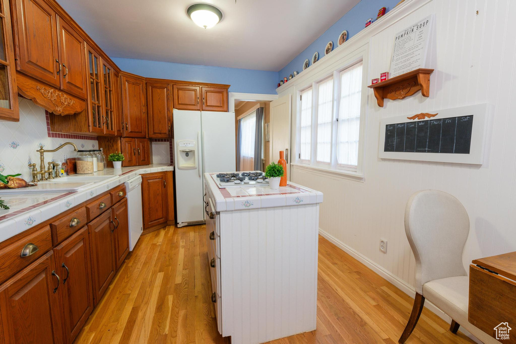 Kitchen featuring light hardwood / wood-style floors, tile countertops, a kitchen island, and white appliances