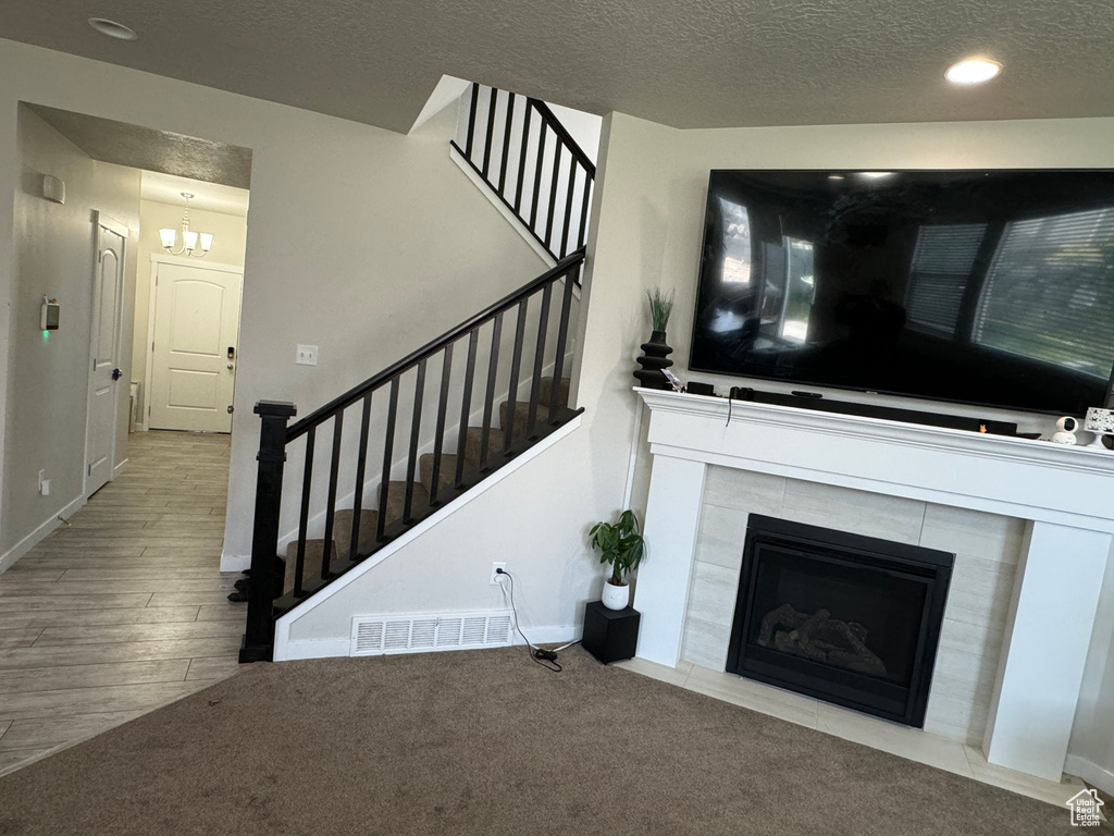 Unfurnished living room with a tiled fireplace, a textured ceiling, an inviting chandelier, and light wood-type flooring
