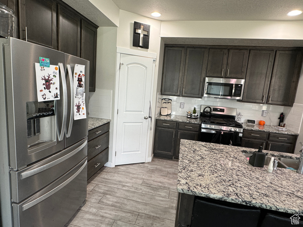 Kitchen featuring stainless steel appliances, a textured ceiling, light hardwood / wood-style flooring, and decorative backsplash