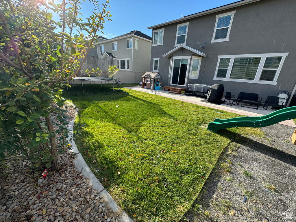Rear view of house with an outdoor living space, a trampoline, a patio area, and a lawn