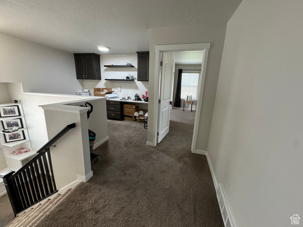 Hall featuring a textured ceiling and dark carpet