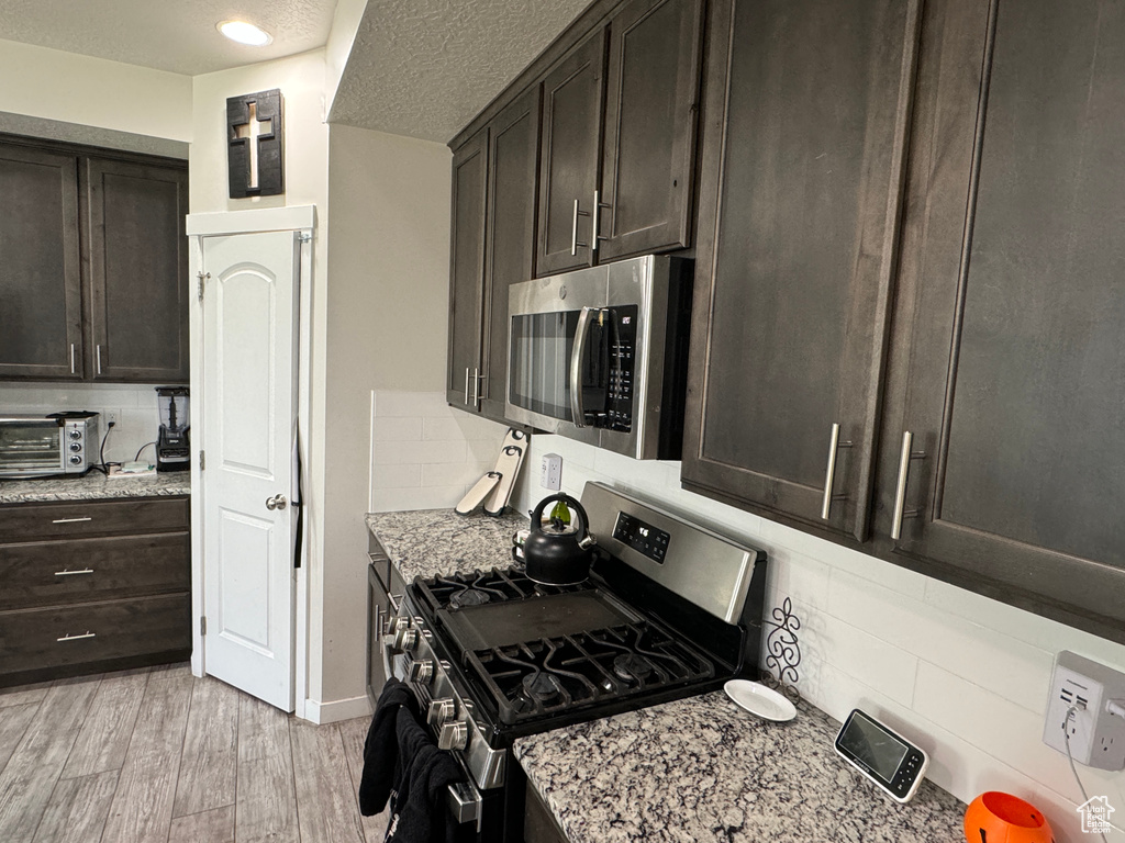 Kitchen with appliances with stainless steel finishes, decorative backsplash, light stone counters, and light hardwood / wood-style floors
