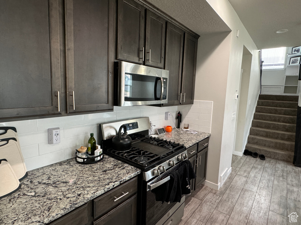Kitchen with stainless steel appliances, dark brown cabinetry, light stone counters, decorative backsplash, and light hardwood / wood-style flooring