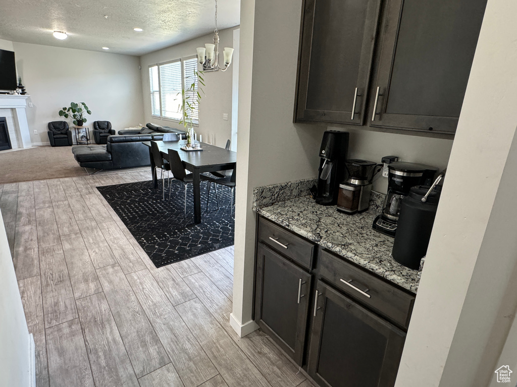 Kitchen featuring a chandelier, light stone counters, dark brown cabinets, and light wood-type flooring