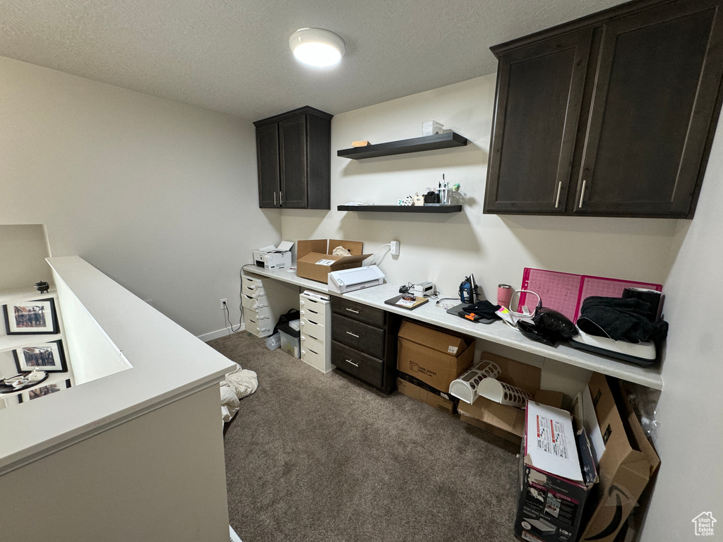 Carpeted home office with a textured ceiling and built in desk