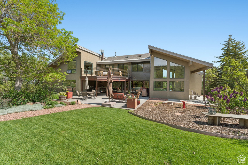 Rear view of house with a balcony, a patio area, stucco siding, and a yard