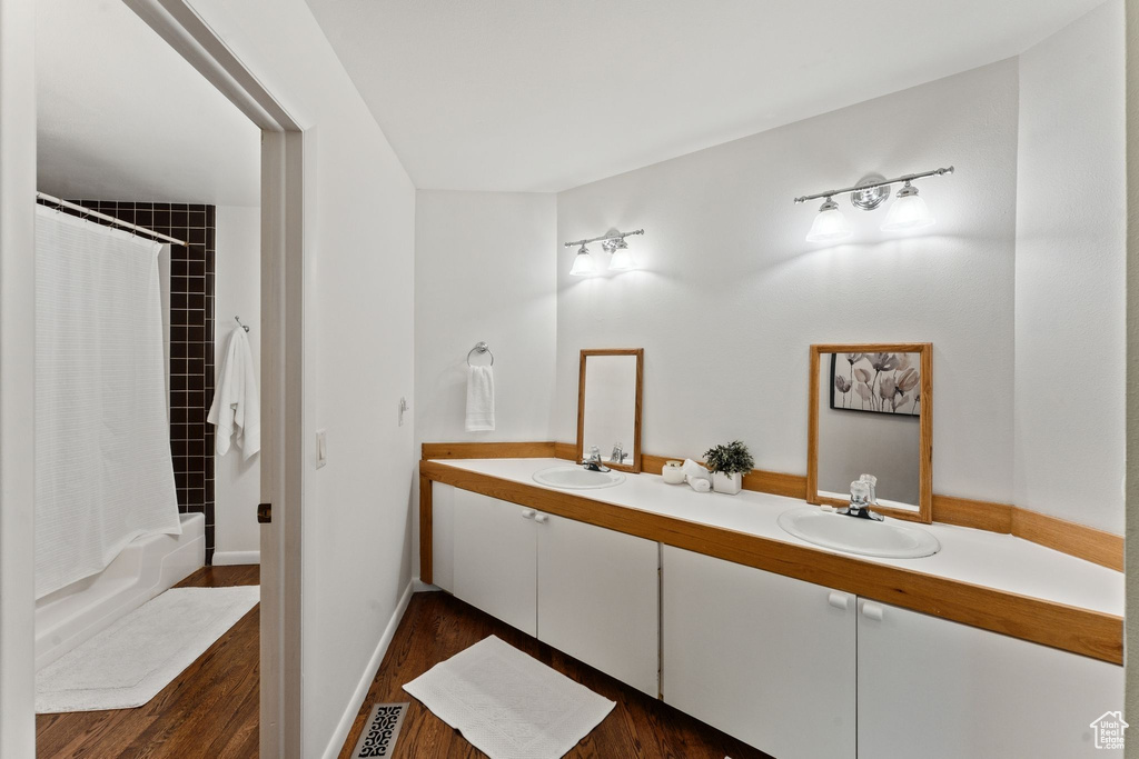 Full bath featuring double vanity, wood finished floors, and shower / bath combination with curtain