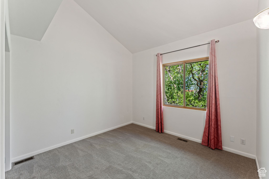 Carpeted empty room featuring lofted ceiling and baseboards
