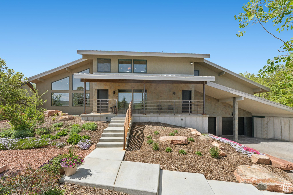 View of front of home featuring covered porch, stucco siding, an attached carport, and stairs