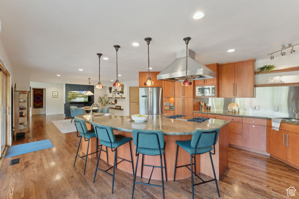 Kitchen with stainless steel appliances, light stone counters, light wood-style flooring, a spacious island, and recessed lighting