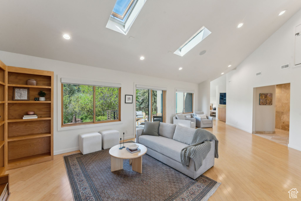 Living room with a skylight, high vaulted ceiling, light wood-style floors, recessed lighting, and baseboards