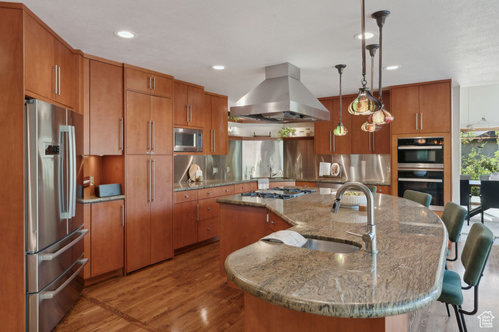 Kitchen featuring appliances with stainless steel finishes, island exhaust hood, a sink, brown cabinetry, and recessed lighting