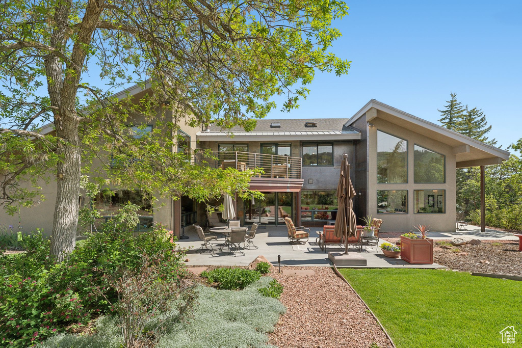 Rear view of property featuring a patio, a balcony, stucco siding, and a yard