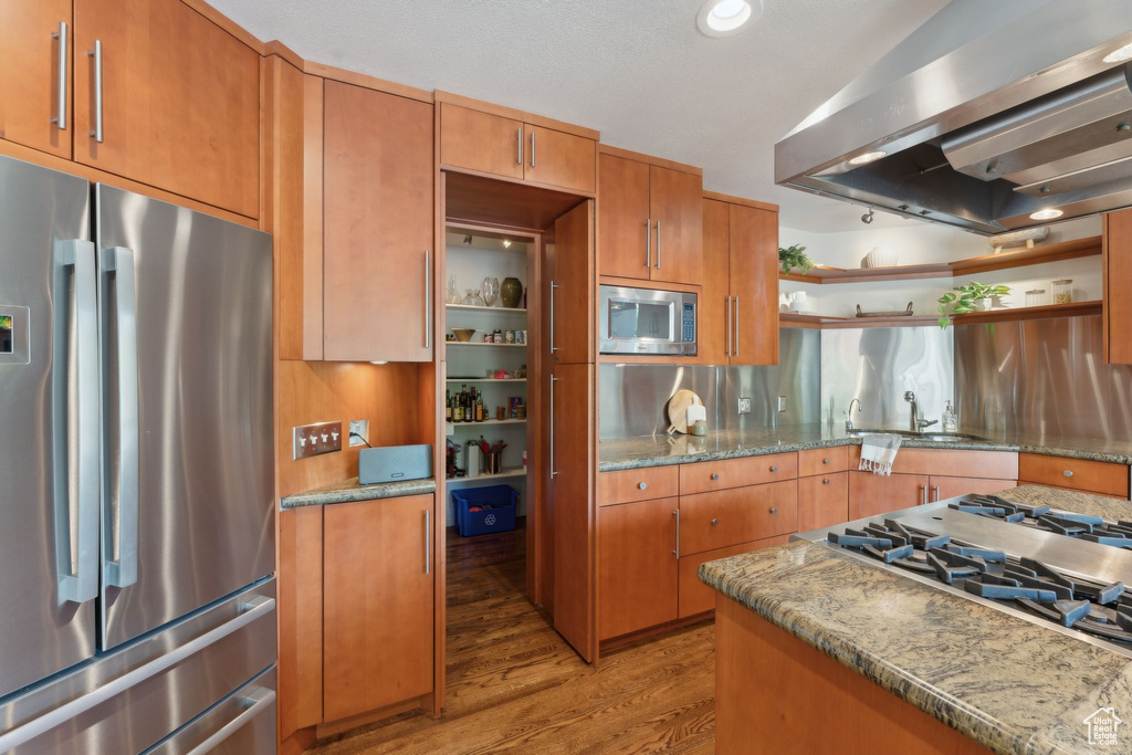 Kitchen featuring stainless steel appliances, wall chimney exhaust hood, open shelves, light wood-style floors, and a sink