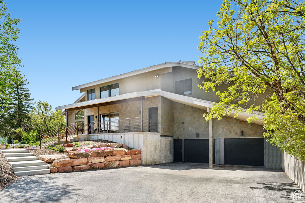 Contemporary home featuring driveway, stucco siding, stone siding, and stairway