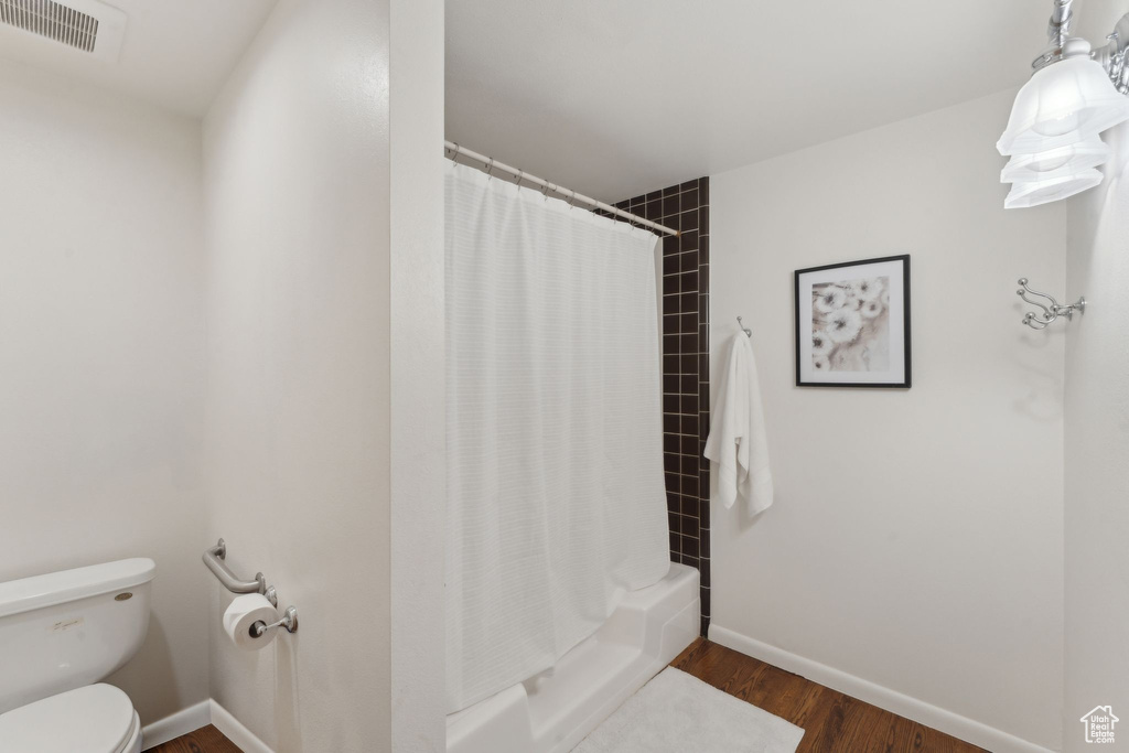 Bathroom with toilet, wood finished floors, baseboards, and shower / bath combo with shower curtain