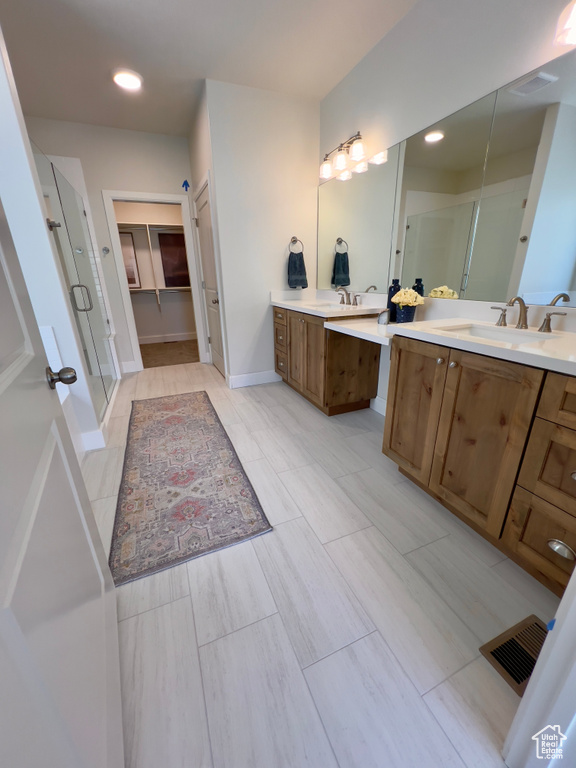 Full bath with a stall shower, two vanities, baseboards, a walk in closet, and recessed lighting