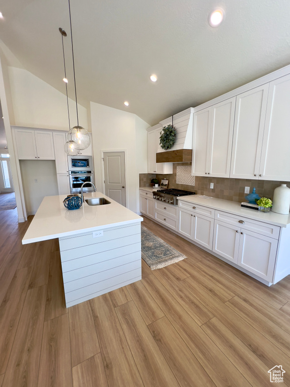 Kitchen with appliances with stainless steel finishes, vaulted ceiling, premium range hood, a sink, and white cabinetry