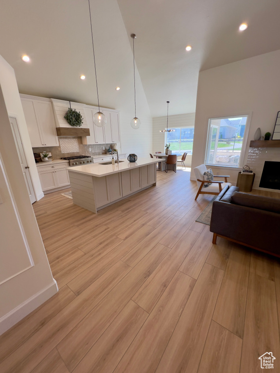 Kitchen with light countertops, decorative backsplash, a center island with sink, white cabinetry, and light wood finished floors