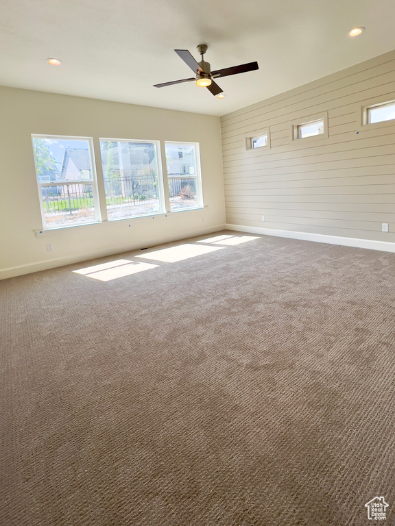 Carpeted empty room featuring baseboards, healthy amount of natural light, a ceiling fan, wooden walls, and recessed lighting