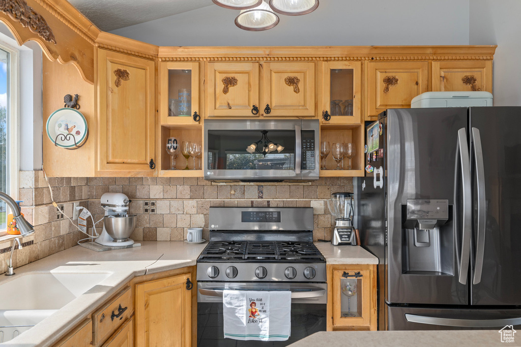 Kitchen with appliances with stainless steel finishes, lofted ceiling, decorative backsplash, and sink