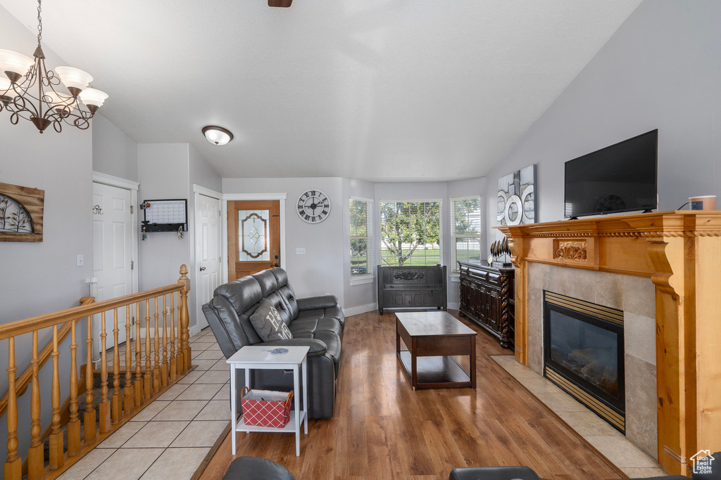 Living room featuring a tiled fireplace, light hardwood / wood-style floors, lofted ceiling, and an inviting chandelier