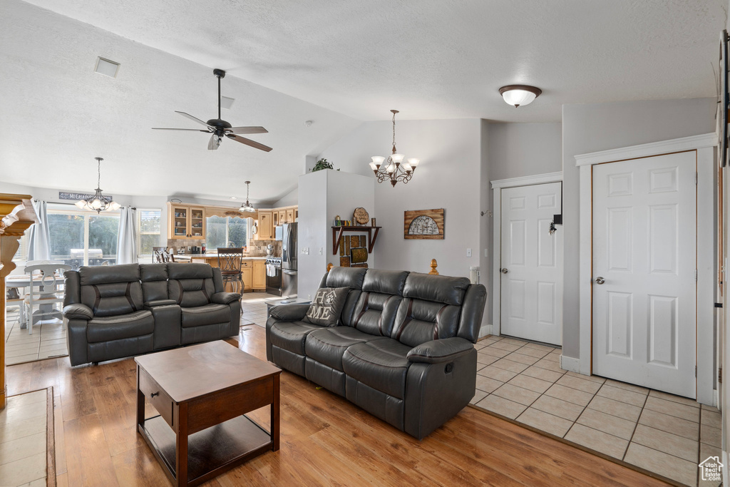 Living room featuring light hardwood / wood-style floors, a textured ceiling, vaulted ceiling, and ceiling fan with notable chandelier