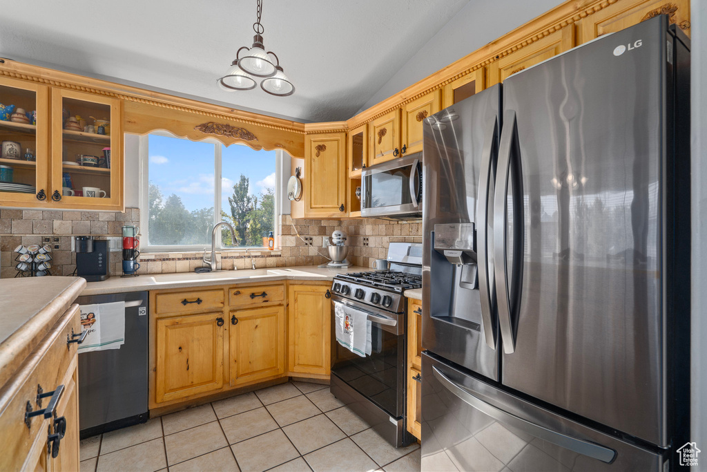 Kitchen with lofted ceiling, hanging light fixtures, stainless steel appliances, backsplash, and light tile patterned floors