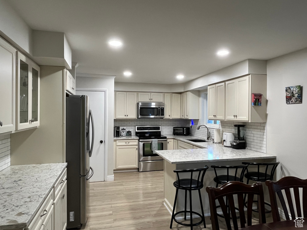 Kitchen with kitchen peninsula, a breakfast bar area, light wood-type flooring, sink, and stainless steel appliances