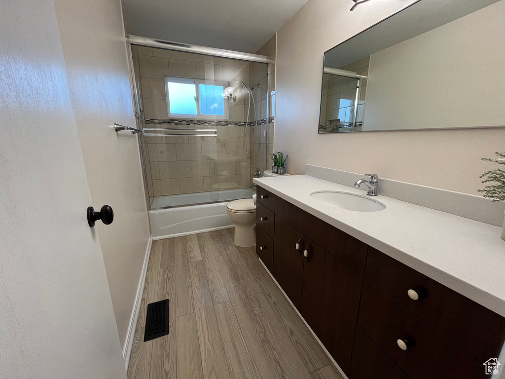 Full bathroom featuring toilet, enclosed tub / shower combo, hardwood / wood-style flooring, and vanity