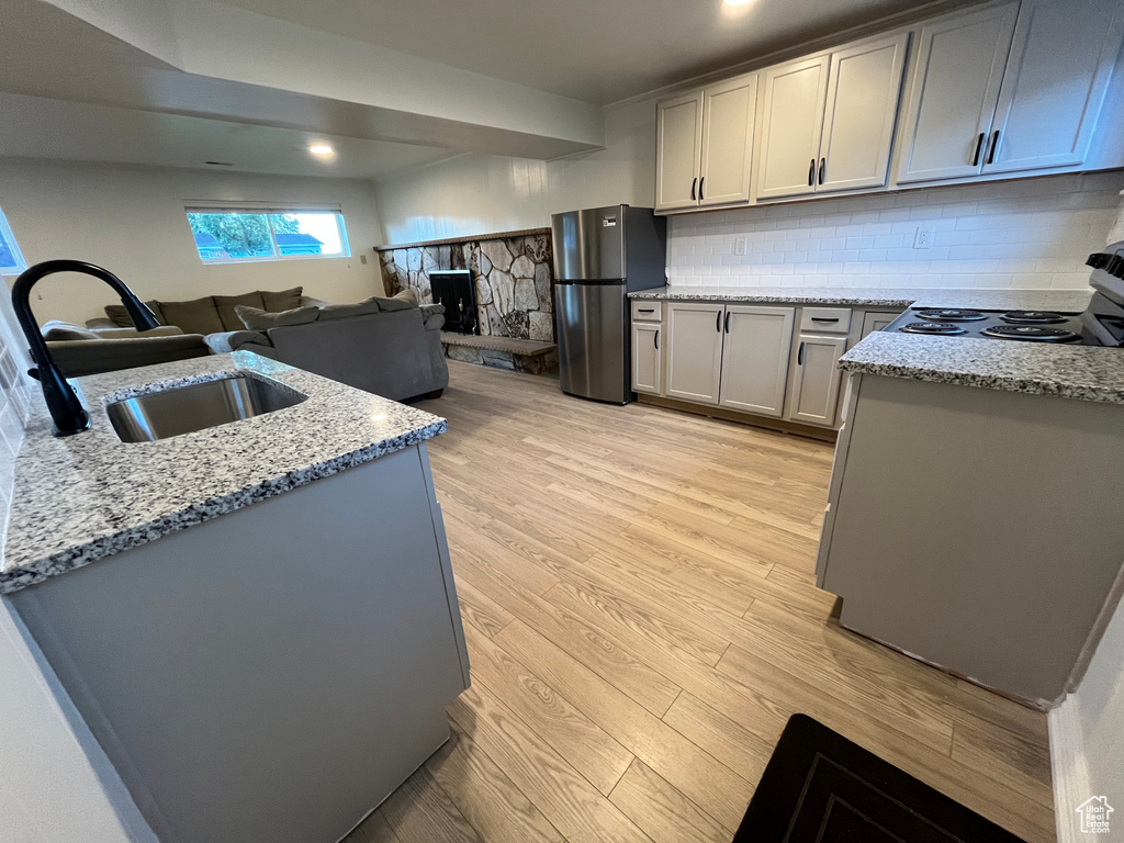 Kitchen featuring stainless steel refrigerator, range, light stone counters, light hardwood / wood-style floors, and tasteful backsplash