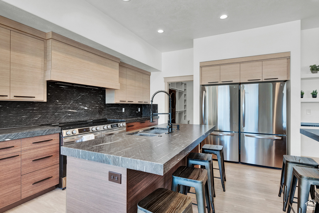 Kitchen featuring a kitchen bar, tasteful backsplash, stainless steel appliances, sink, and a center island with sink