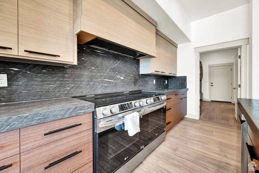 Kitchen with light hardwood / wood-style floors, premium range hood, tasteful backsplash, and stainless steel stove