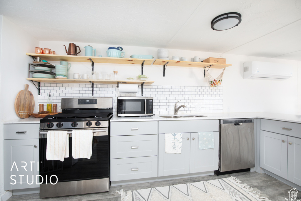 Kitchen with appliances with stainless steel finishes, sink, backsplash, light hardwood / wood-style floors, and a wall mounted AC