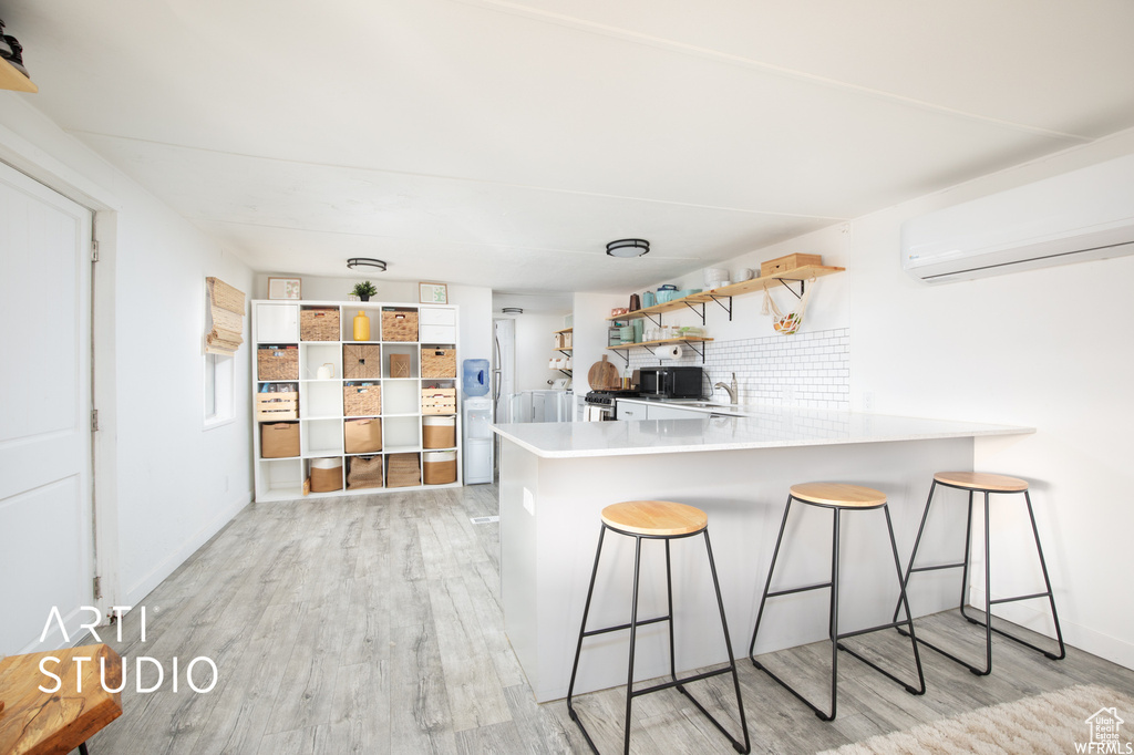 Kitchen with an AC wall unit, kitchen peninsula, backsplash, a kitchen bar, and light hardwood / wood-style floors