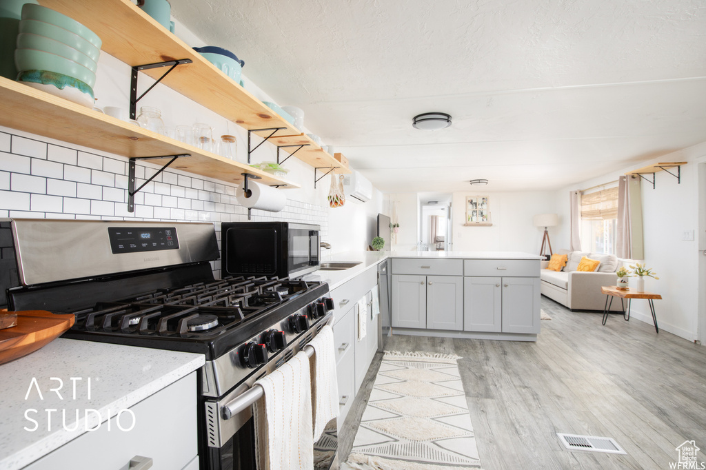 Kitchen featuring kitchen peninsula, backsplash, appliances with stainless steel finishes, gray cabinetry, and light hardwood / wood-style floors