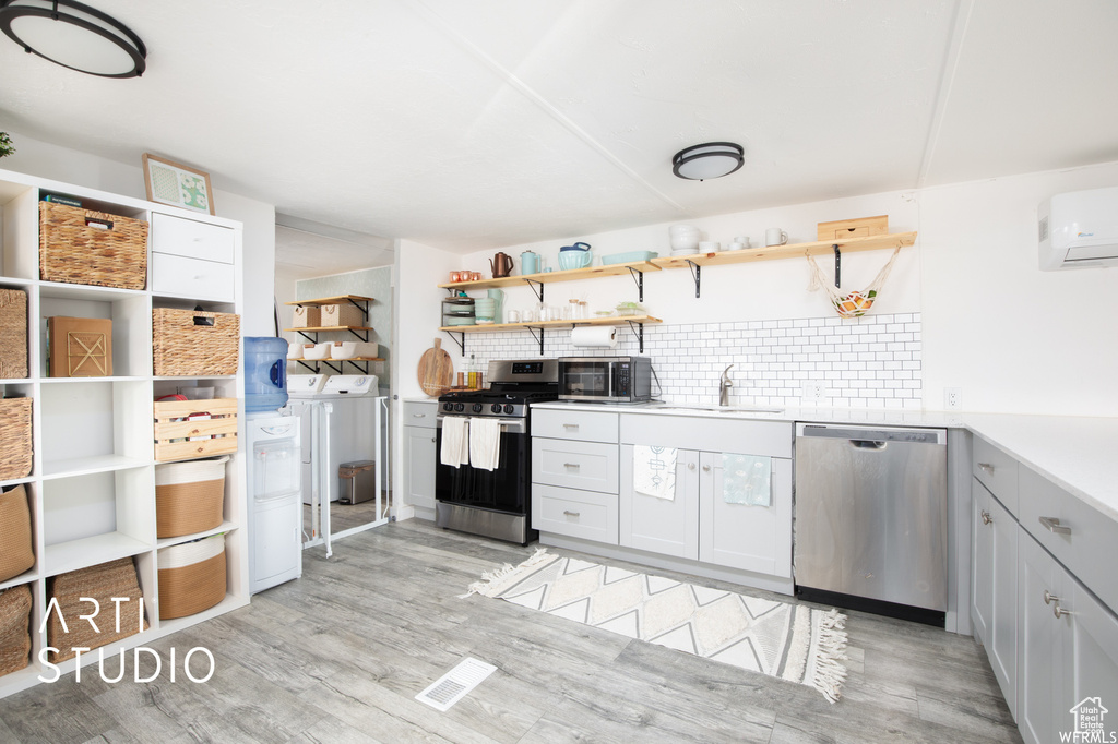 Kitchen featuring decorative backsplash, appliances with stainless steel finishes, washer and dryer, light hardwood / wood-style flooring, and sink